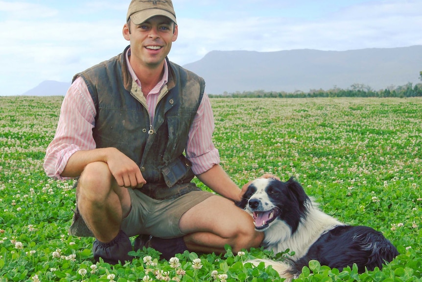 a farmer squats in a paddock of clover with his dog