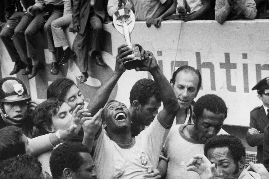 Pele is lifted and looks up at the world cup trophy