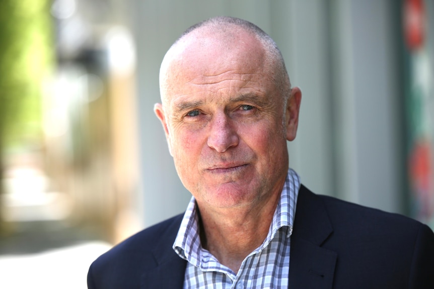 A man wearing a jacket and a collared shirt looks seriously at the camera. 