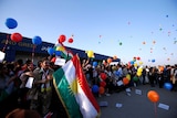 Kurdis protest outside the Erbil International Airport. They are smiling holding flags and releasing bright coloured balloons