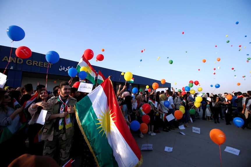 Kurdis protest outside the Erbil International Airport. They are smiling holding flags and releasing bright coloured balloons