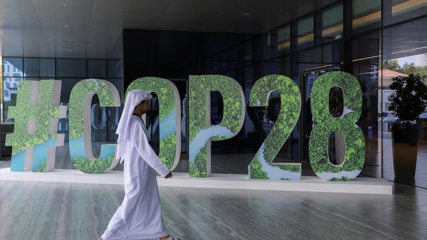 Wide shot of a person walking in front of a sign reading COP28.