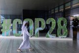 Man wearing traditional Emirati clothing walks past a big saying which reads #COP28