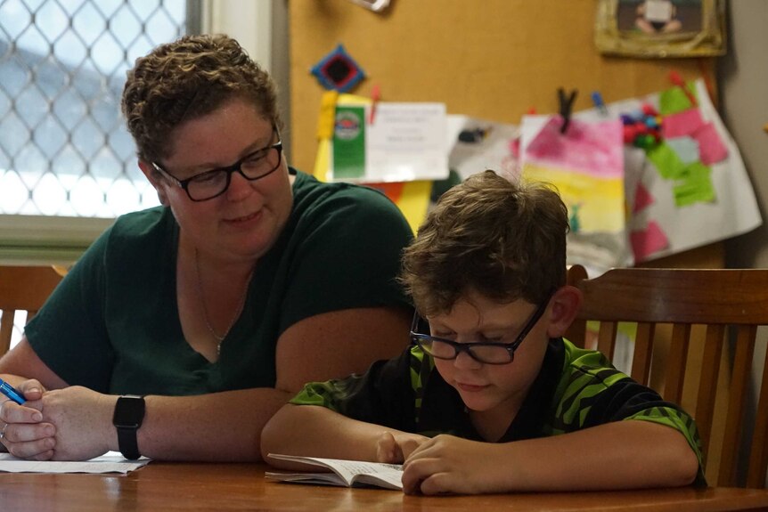 Berry Springs mum Naomi Hunter and her son sit at a table inside and read a book.