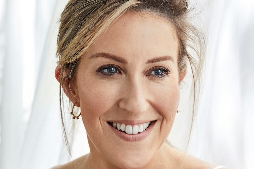 A woman smiles for a professional headshot. She has blonde hair and blue eyes