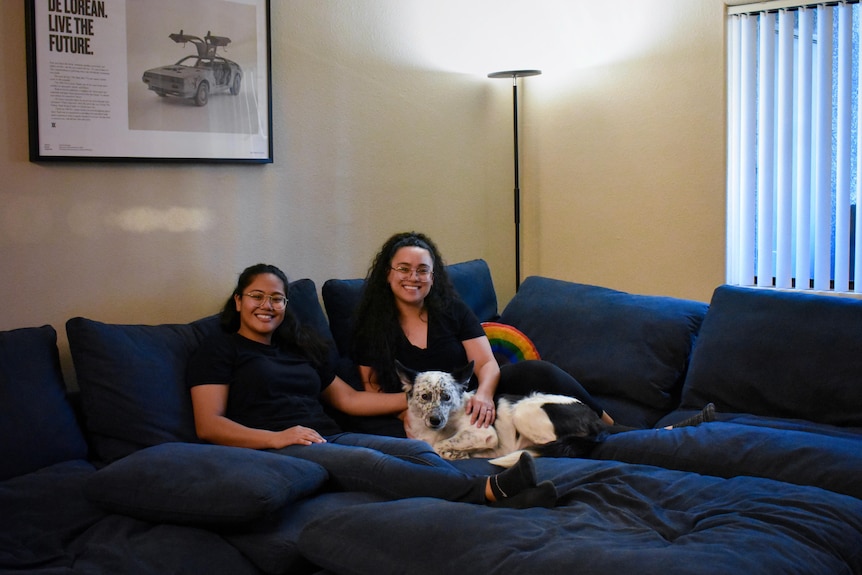 Angely Ventura and Taylor Cunanan sit on the couch with Luna, their dog