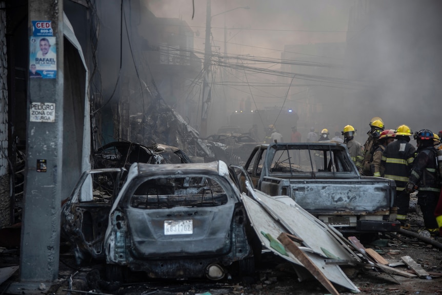 Firefighters work next to burnt out vehicles surrounded by rubble