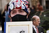 A mourner holds up a photo of Prince Philip and Queen Elizabeth II and a bouqet of flowers