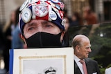 A mourner holds up a photo of Prince Philip and Queen Elizabeth II and a bouqet of flowers