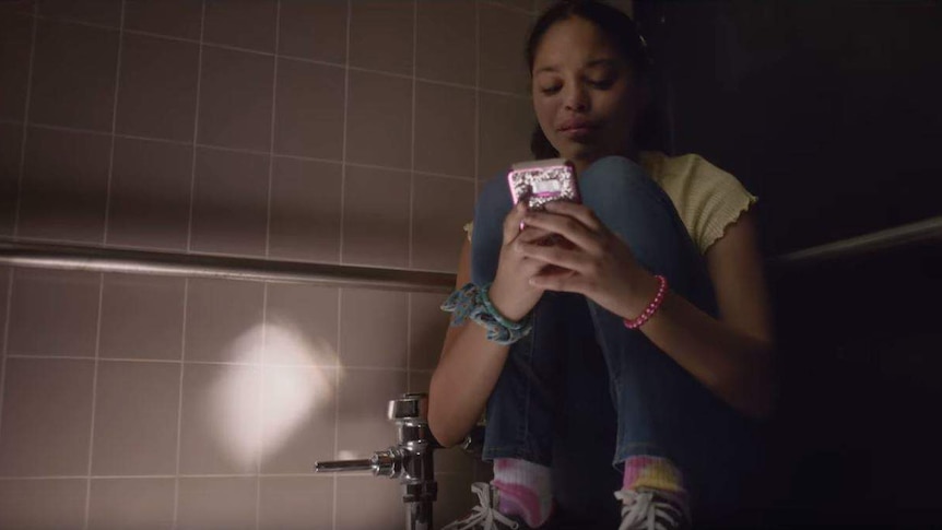 A girl squats on a toilet looking at her phone in a scene from an anti-school-shooting PSA.