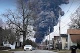 A giant plume of smoke bellows in background of a suburban street. 
