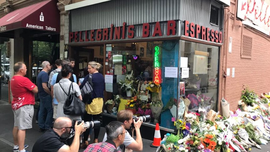 Half a dozen customers stand outside Pellegrini's Espresso Bar as other people photograph floral tributes along the wall.