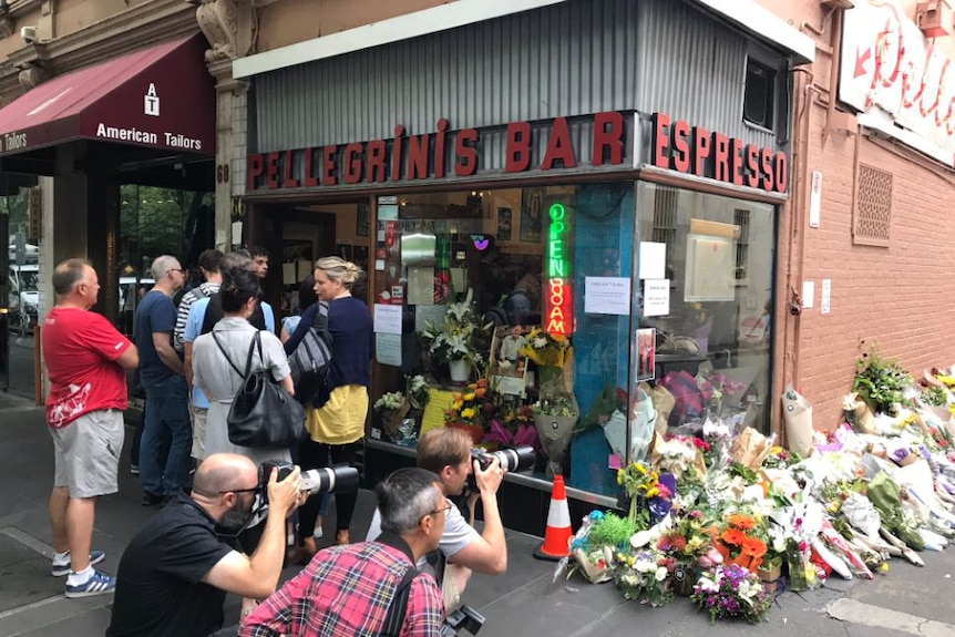 Half a dozen customers stand outside Pellegrini's Espresso Bar as other people photograph floral tributes along the wall.