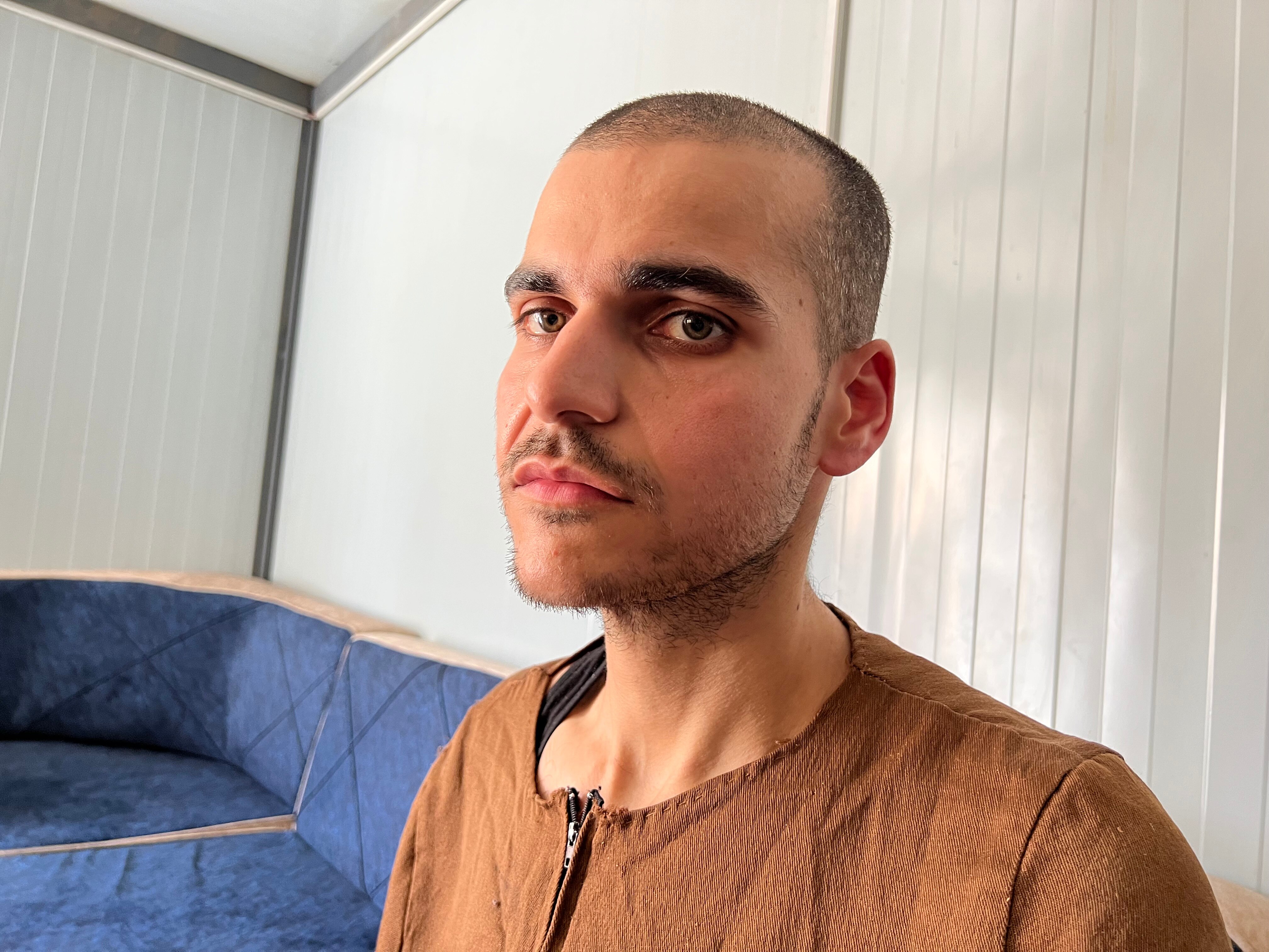 A gaunt man in brown prison garb stares into the distance