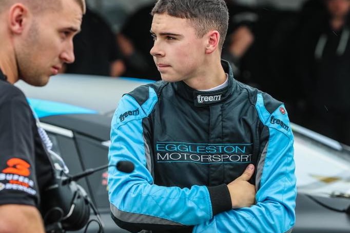 A young man dressed in blue and black motor racing gear