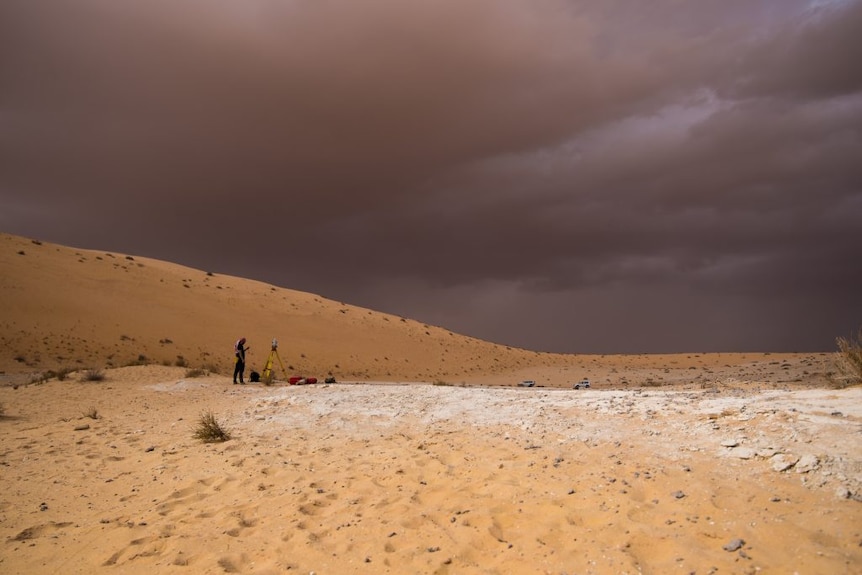 A man stands in the middle of a desert with surveying equipment