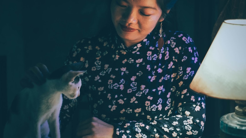 A woman in a floral shirt strokes a white cat.