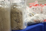 Two large jars of heroin sit on a table in plastic bags.