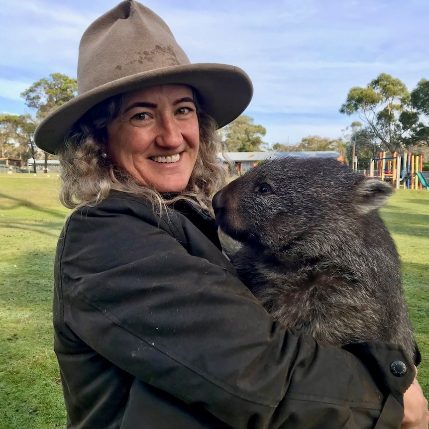 A woman in a hat holds a small wombat called George.
