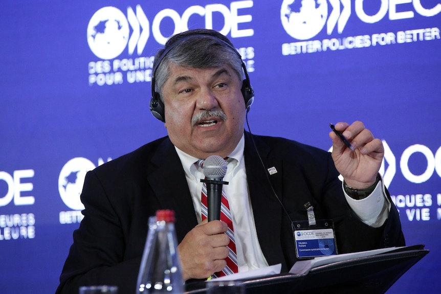 A man gestures while speaking at a lectern