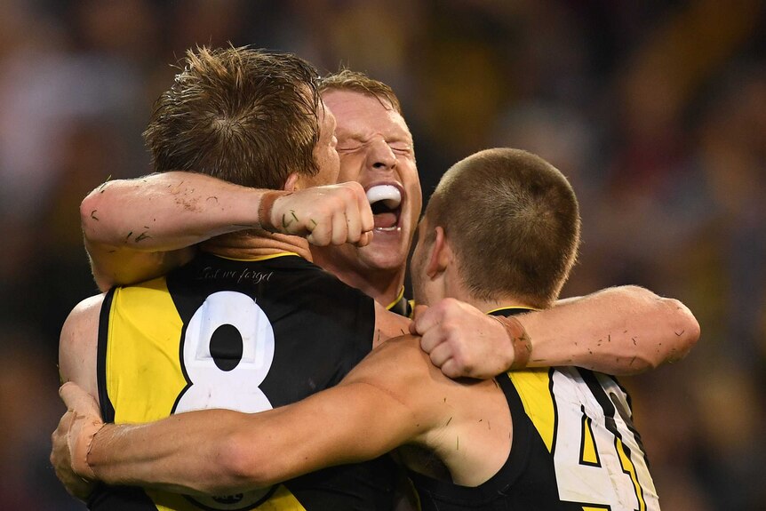 Richmond's Josh Caddy hugs two Tigers players after kicking a goal during Round 5 against the Demons.