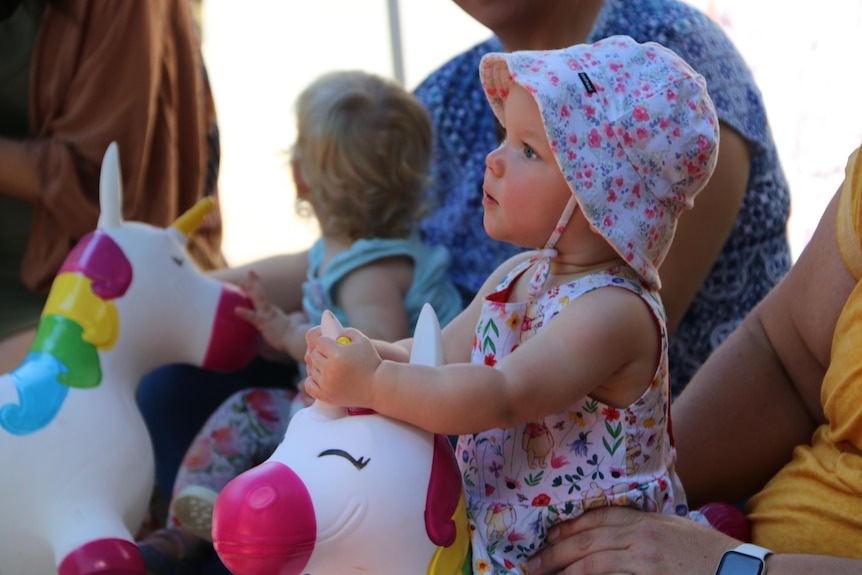 Lucy wearing a floral hat holds the ears of a blow up unicorn.