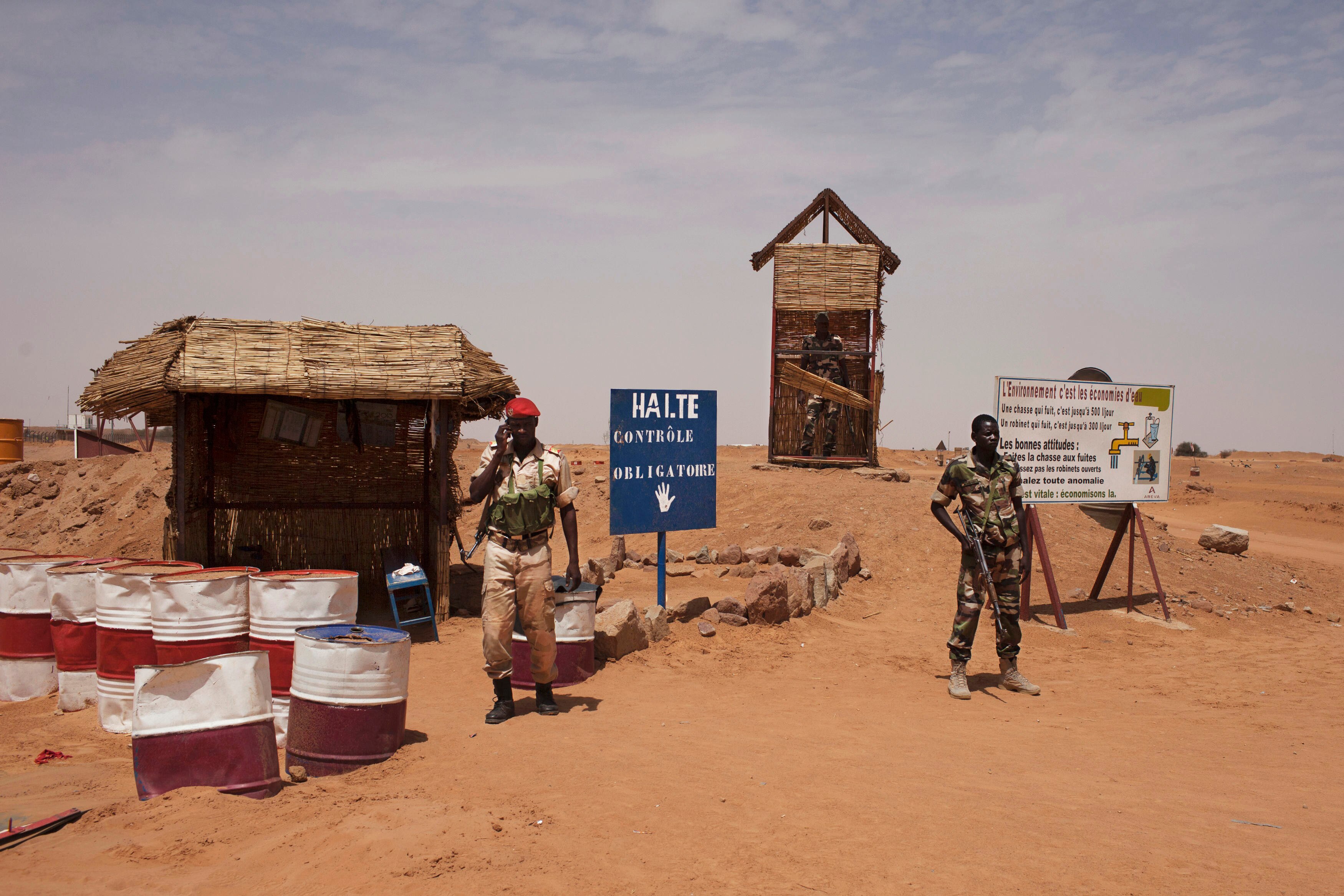Two men in army gear holding guns stand in front of a sign reading Halte.