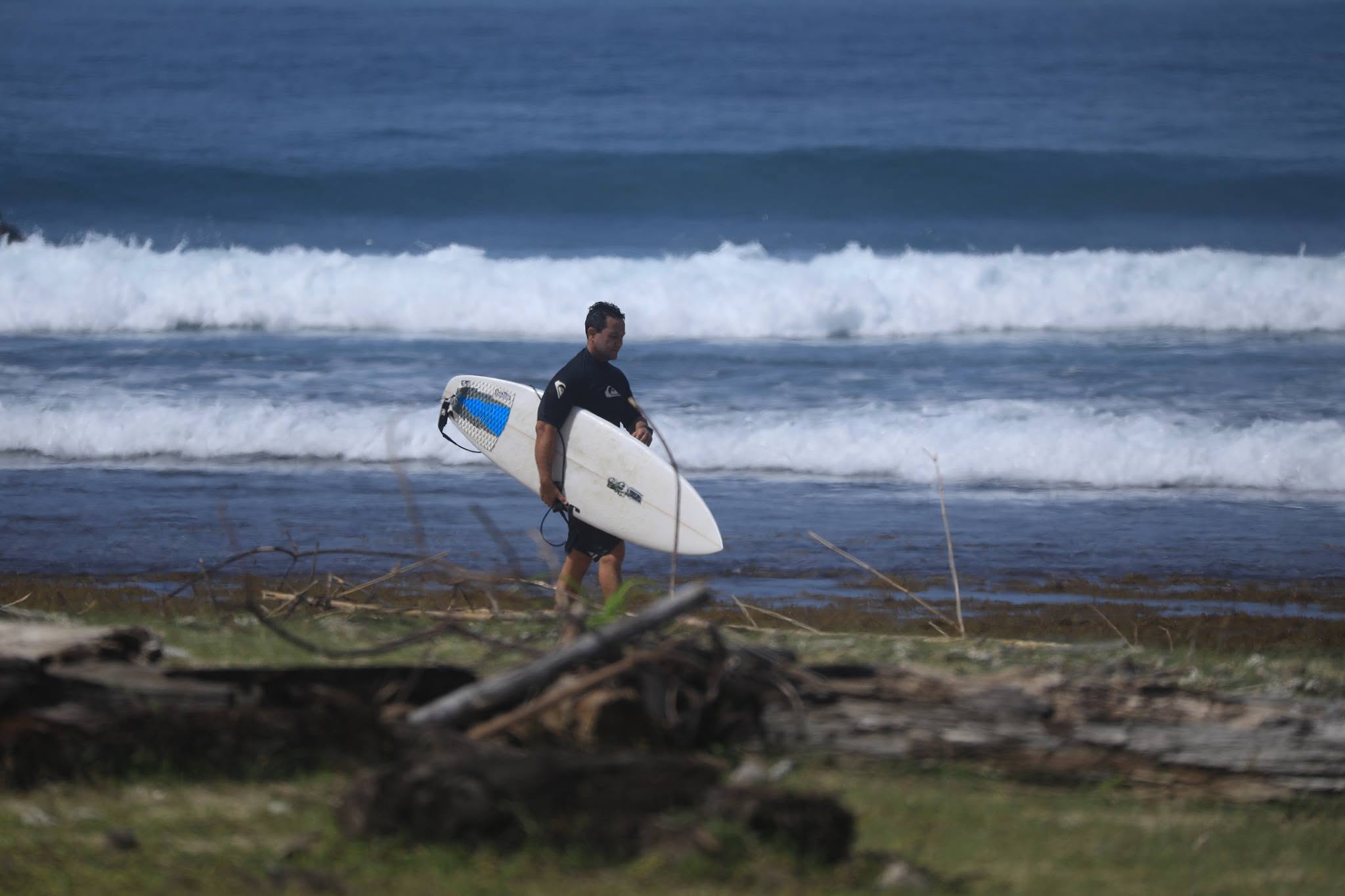 A man in wet suit is carrying his surfboard at the beach.