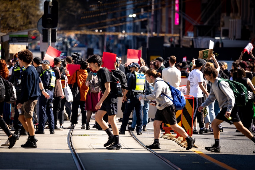 Protesters cross tram tracks in Melbourne on a sunny day.