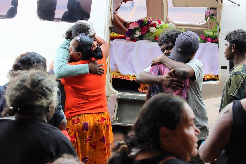 People embrace outside an airplane that has the coffin of Mr Yunupingu on board.