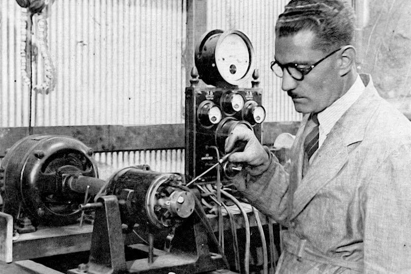 A man wearing glasses works on an electrical device taken on a old camera. 