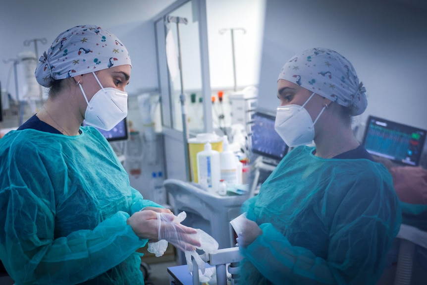 A female health worker in blue scrubs puts on rubber globes in a ward