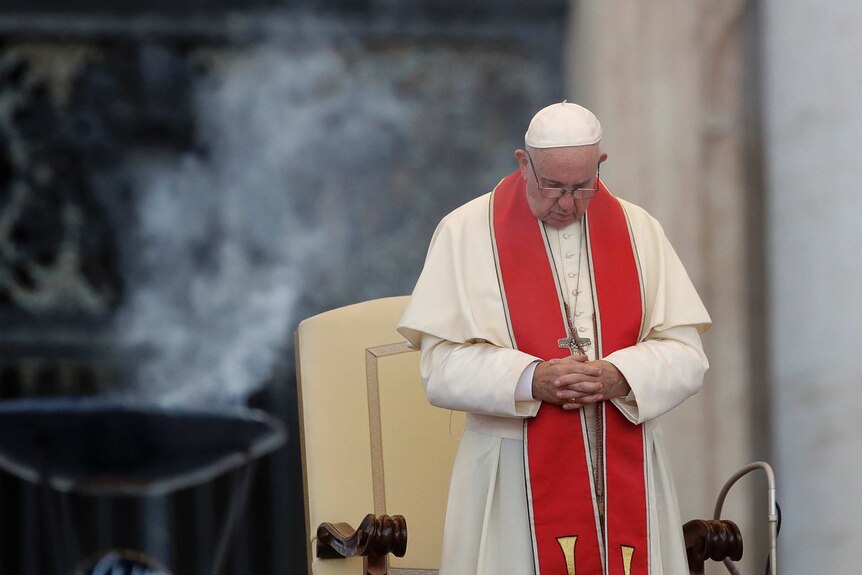 Pope Francis prays with his head down and hands clasped.