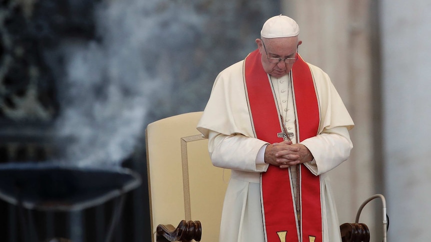 Pope Francis prays with his head down and hands clasped.