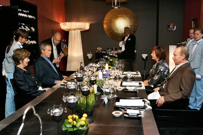 George Bush, Laura Bush, Vladimir Putin and Lyudmilla Putina sit opposite each other at a lavish dinner table in a restaurant