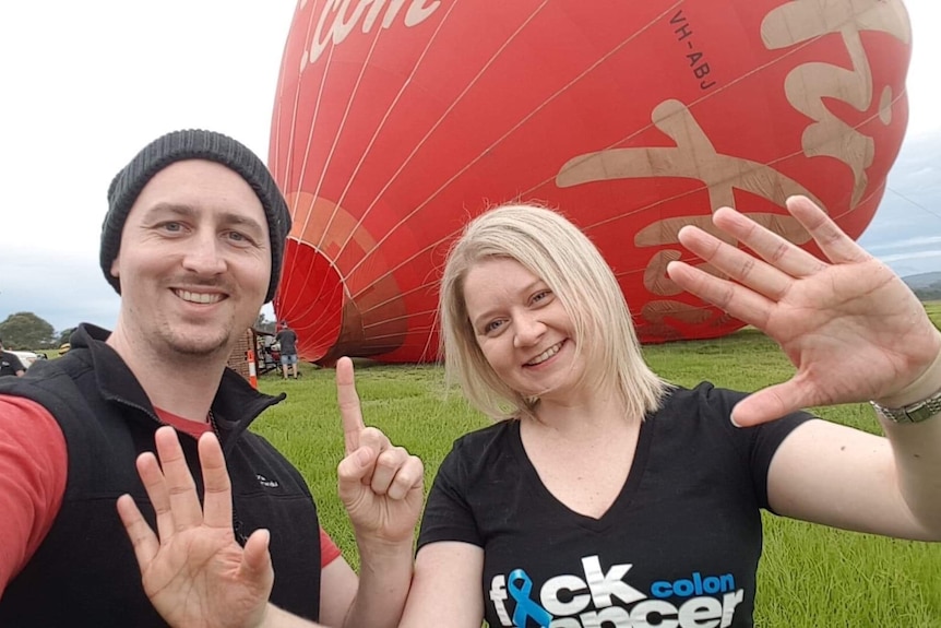 Ken Simpson and Katherine Goodall stand in front of a hot air balloon, holding up 11 fingers