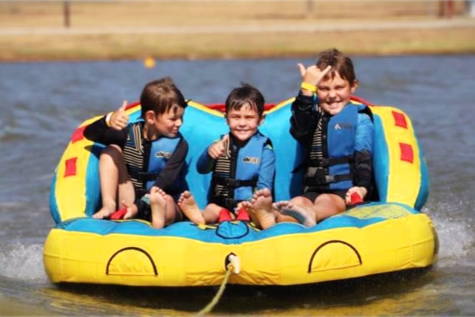 three young boys laugh as they sit on an inflatable out on a lake