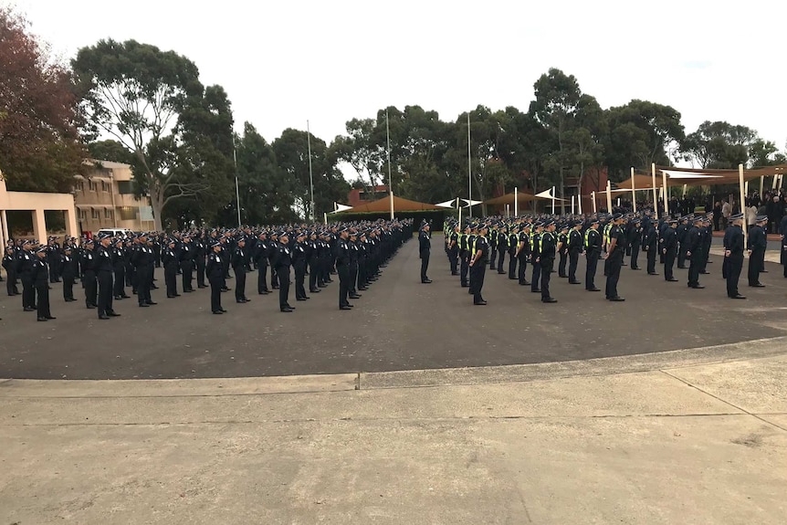 Police officers and protective services officers stand at attention on a concrete oval.