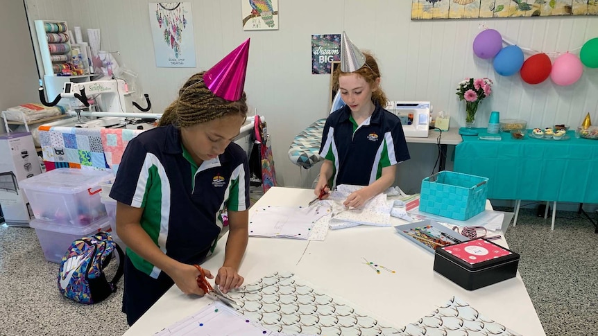 Two girls stand at a table cutting out patterns