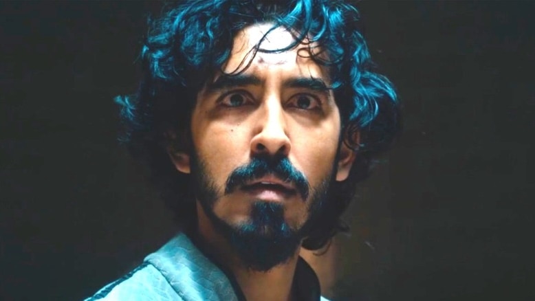 A man with dark curly hair and a beard and moustache looking past the camera fearfully.