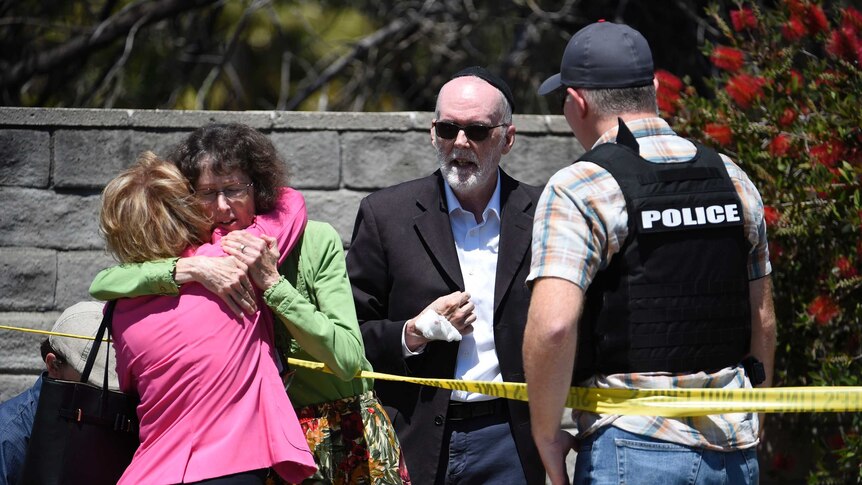 Two people hug as another talks to a San Diego County Sheriff's deputy outside of a Synagogue