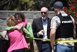 Two people hug as another talks to a San Diego County Sheriff's deputy outside of a Synagogue