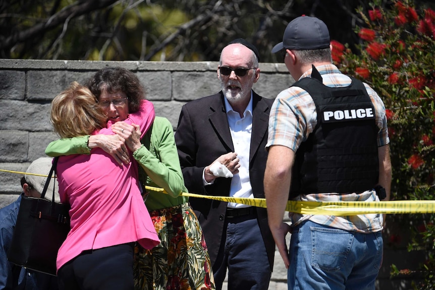 Two people hug as another talks to a San Diego County Sheriff's deputy outside of a Synagogue