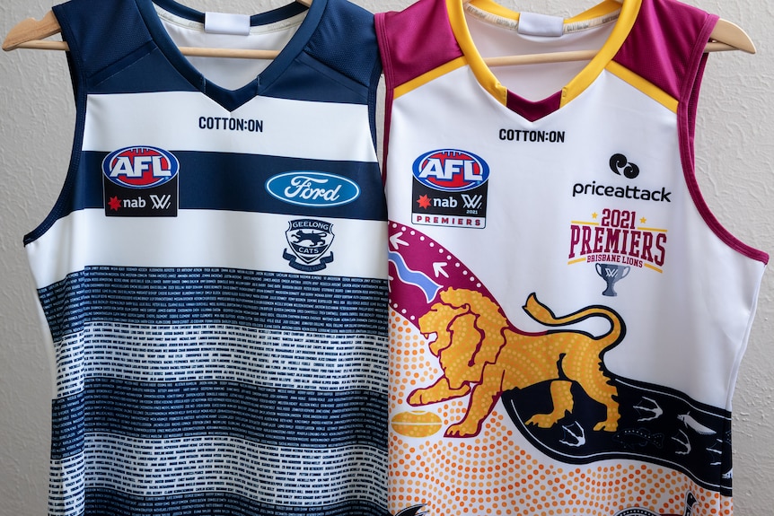A Brisbane Lions jersey and a Geelong Cats jersey hang side by side on coat hangers.