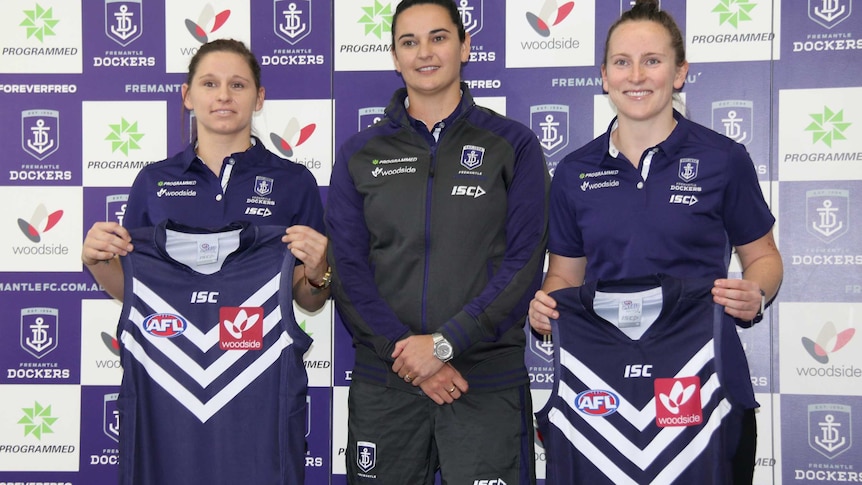 Fremantle Dockers women's players Kiara Bowers and Kara Donnellan stand either side of coach Michelle Cowan holding team jumpers