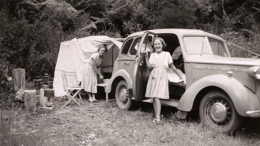 A mother and daughter posing with their family car and tent.