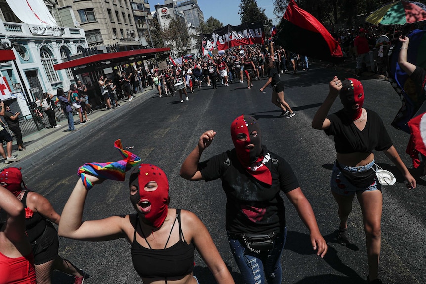 Women in red and black masks shout as they walk down the street during an International Women's Day march in Santiago, Chile.