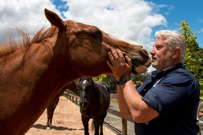 Dean Mighell kisses one of his horses on his property at Trentham, in Central Victoria.