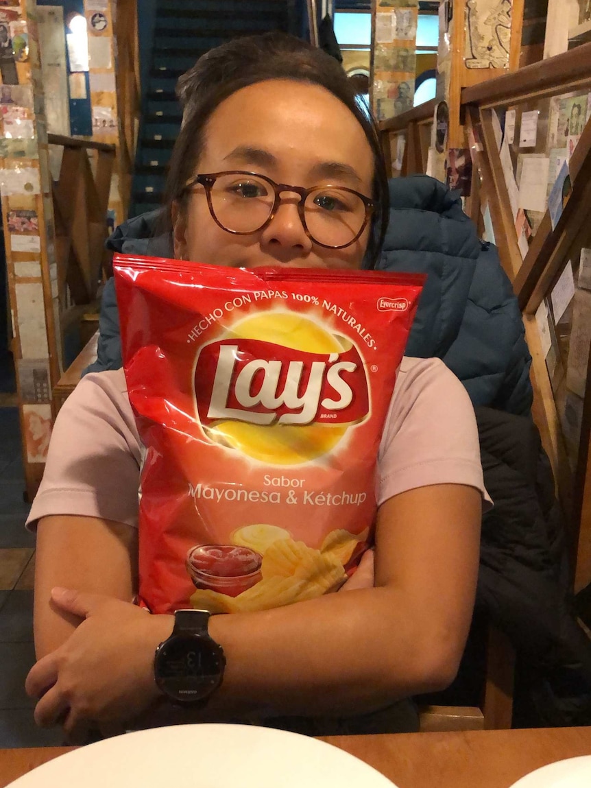 Vicky is hugging a large packet of chips in her arms, with just her eyes showing over the chip packet.