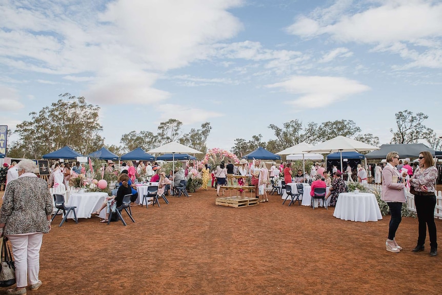 Women gather around decorated tables and umbrellas set up in an outback paddock.